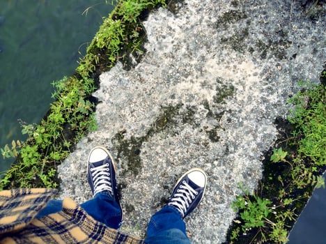 First Person View of Feet in Sneakers Standing on a Mossy Stone Bridge photo