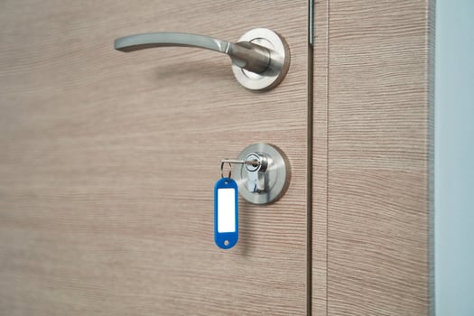 A key with a blank keychain in the lock of a wooden door close up photo