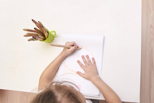 Caucasian child drawing with colored pencils on white paper at wooden desk. photo