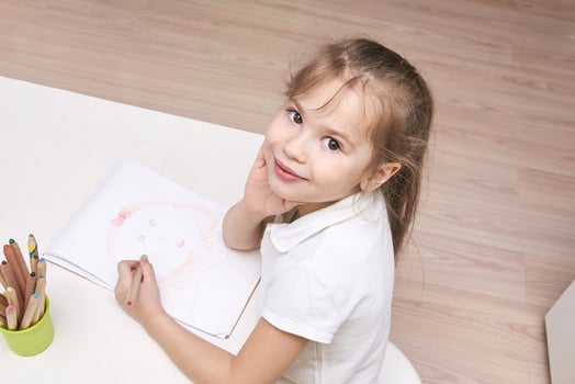Caucasian female child smiling and drawing at table with colored pencils in bright room. photo