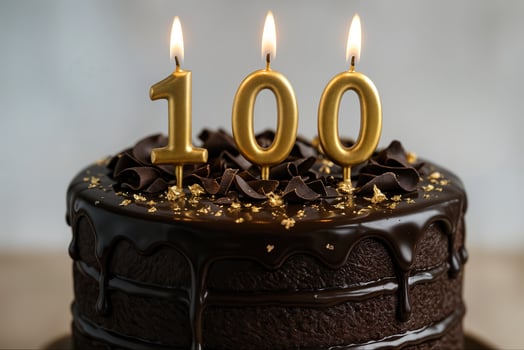 Centennial Chocolate Cake with Candles Celebrating 100th Birthday Anniversary Surrounded by Elegant Gold Decorations and Rich Dark Icing Dripping Down Sides Symbolizing Century Milestone photo
