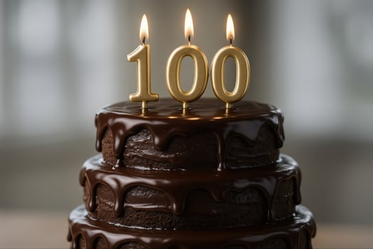 Elegant Centennial Chocolate Cake With Dripping Icing and Golden Candle Numbers Celebrating 100 Years Milestone on Tiered Dessert for Special Occasions and Anniversaries photo