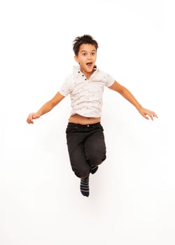 Young boy with dark hair and casual clothes is jumping with an excited expression, isolated on a white background. Suitable for concepts related to childhood, energy, happiness, and playful activities. photo