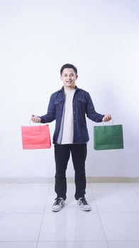 Full length photo of smiling Asian man holding shopping bags in both hands isolated on white background