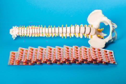 Many red pills in blisters against the background of a model of a human spine and a blue background. Concept of treating the spine with chondroprotector pills and homeopathy, close-up photo