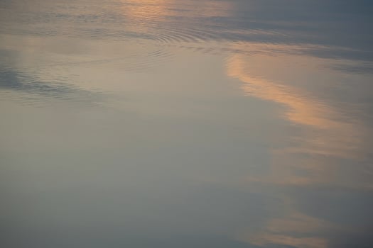 Reflection of orange sky clouds and ripples on calm lake surface during twilight photo