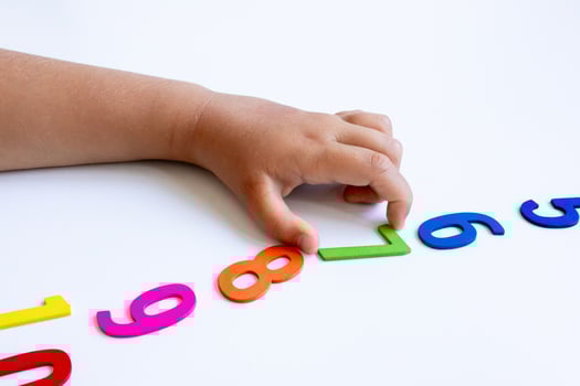 Child hand arranging colorful wooden numbers on white surface photo