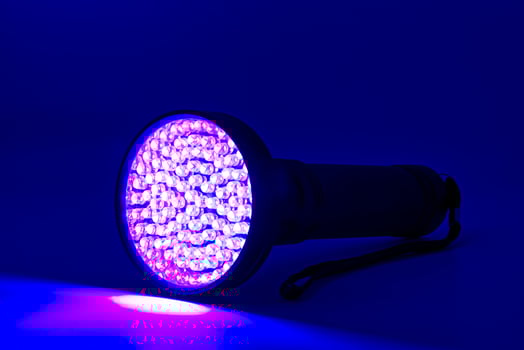 A powerful ultraviolet flashlight with numerous small led bulbs casting a vibrant purple glow on a dark blue surface. photo
