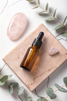 Amber glass dropper bottle with rose quartz and eucalyptus on marble surface photo
