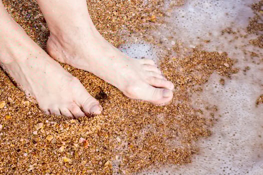 Bare feet standing on sandy beach, gentle wave washing the shore, serene moment of relaxation by the sea photo