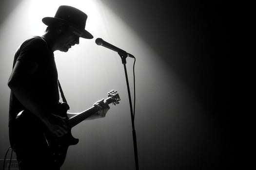 A man in a hat playing guitar in front of a spotlight photo