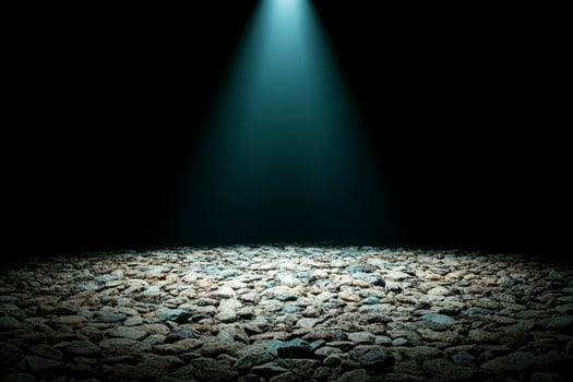 A dark room with a spotlight shining on a gravel floor photo