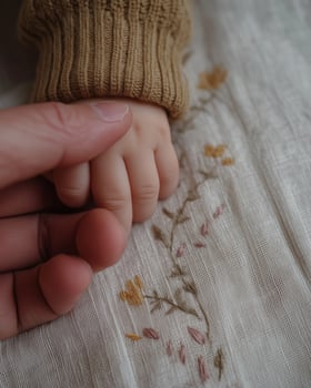 Adult Hand Holding Baby Hand on Embroidered Fabric photo