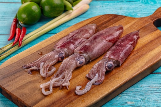 Three squid on a cutting board with lime and other vegetables photo