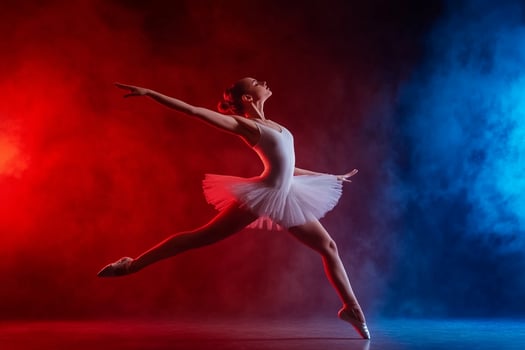 A young ballerina in a white dress is dancing in front of a red and blue smoke photo