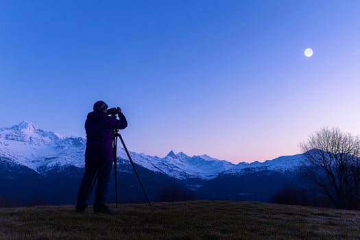 A man taking a photo of the moon with a mountain in the background