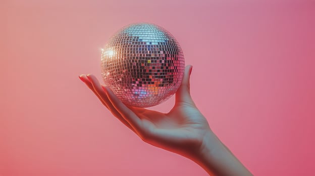 Hand Holding a Shiny Disco Ball Against a Vibrant Pink Background During a Bright Day. photo
