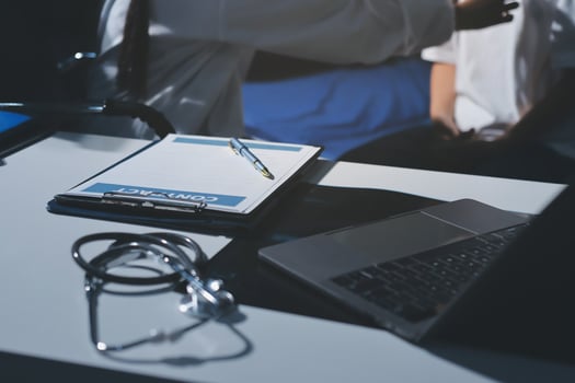 A laptop and clipboard on a desk with a doctor photo
