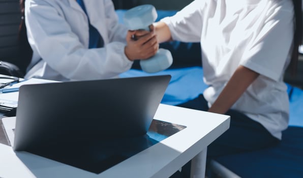 A doctor is working on a laptop while a woman sits on a bed photo