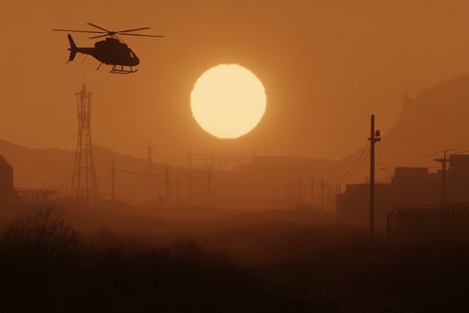 A helicopter flying over a field with a sun setting behind it photo