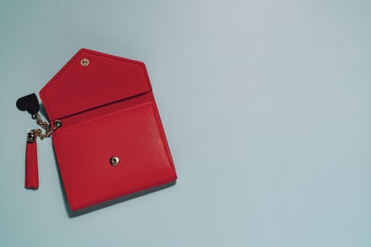 Stylish red wallet, partially open with tassel and heart keychain, on clean blue. Symbolizes personal finance, fashion, accessories, and giving receiving. photo