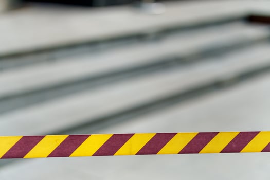 A caution tape with bright yellow diagonal stripes is stretched in front of stairs, indicating a potentially hazardous or restricted area. photo