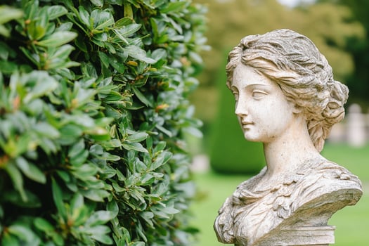 A statue of a woman in front of a hedge photo