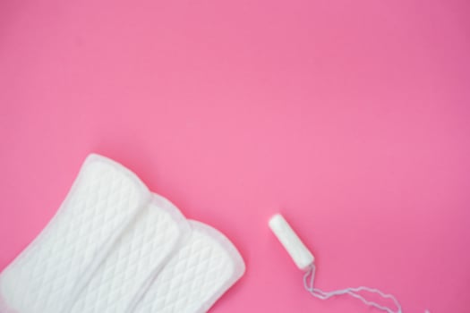 Blurred white sanitary pads and a tampon isolated on a plain pink background. Suitable for topics about feminine hygiene, menstruation, and period care products. photo