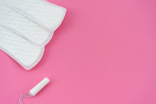 White sanitary pads and a single tampon isolated on a plain pink background. Suitable for topics related to feminine hygiene, menstruation, and women health education. photo