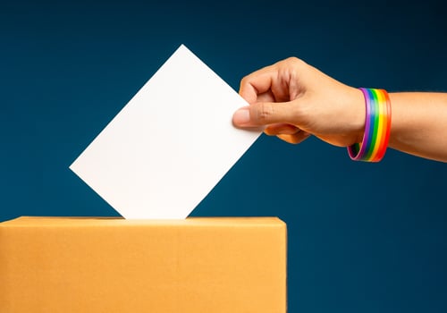 Election day. Close-up of a a hand voter holding ballot paper putting into the voting box at place election against a blue background photo