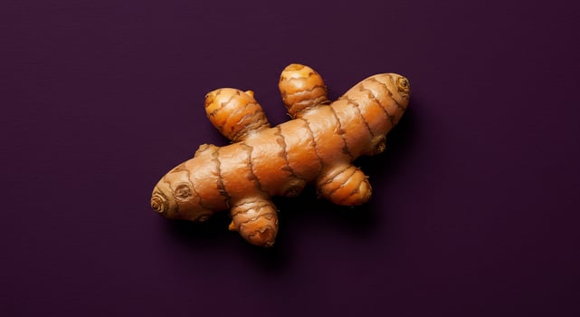 Vibrant yellow-orange turmeric root displayed on a rich purple surface. photo
