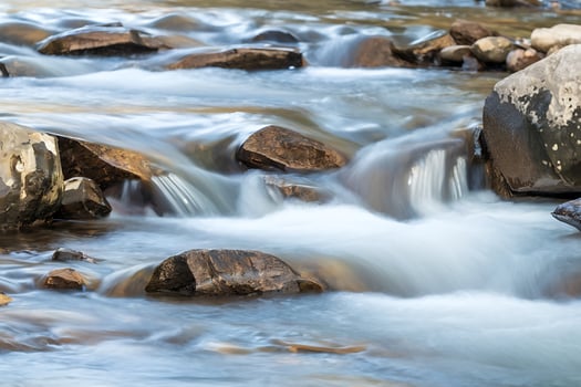 Smooth Water Flowing Over Brown Rocks in a Stream river stones photo