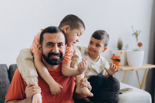 Happy middle eastern f ather having fun with his three sons at home. Dad cuddling toddler while other kids play and smile. Loving family moment on cozy sofa photo