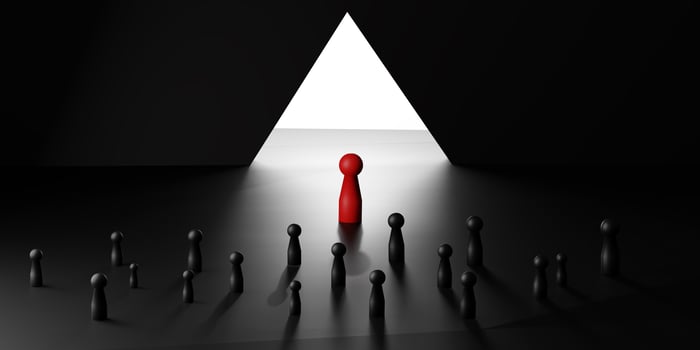 Leadership and innovation symbolized by a red doll standing before a bright triangular light, surrounded by black dolls, representing breakthrough and challenge. photo