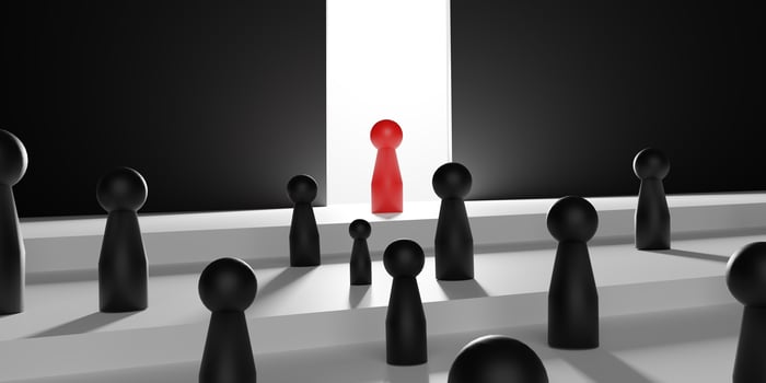 Leadership symbolized by a single red doll standing out among black dolls on a tiered platform, representing uniqueness and the path to success with a bright light ahead. photo