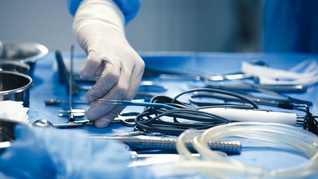 Surgical hand in sterile gloves is carefully selecting instruments from a blue surgical table filled with various medical tools and equipment, showcasing precision in a clinical environment photo