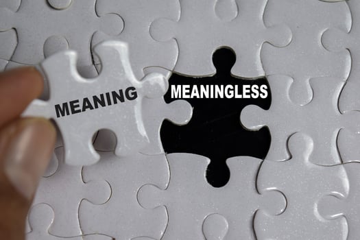 Hand holding piece of jigsaw puzzle with word meaning and meaningless. Business and finance concept photo