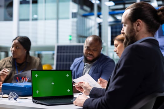 Photovoltaics factory workers analyzing data, reviewing system health metrics with green screen laptop. Solar panels plant employees troubleshooting technical issues using chroma key notebook photo