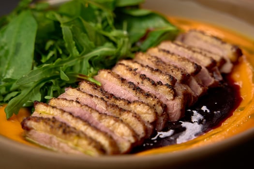 Deliciously Plated Sliced Duck Breast Served on a Bed of Vibrant Carrot Puree with Fresh Greens for a Harmonious Culinary Experience photo