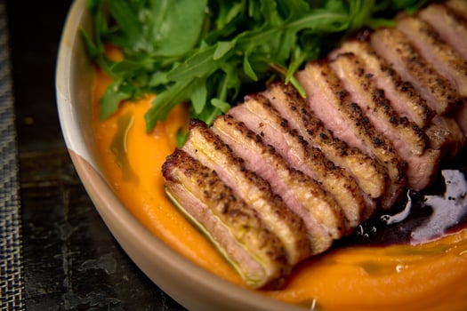 Savory Exquisite Dish Featuring Succulent Slices of Perfectly Cooked Meat Arranged Elegantly Over a Vibrant Sauce and Accompanied by Fresh Green Herbs photo