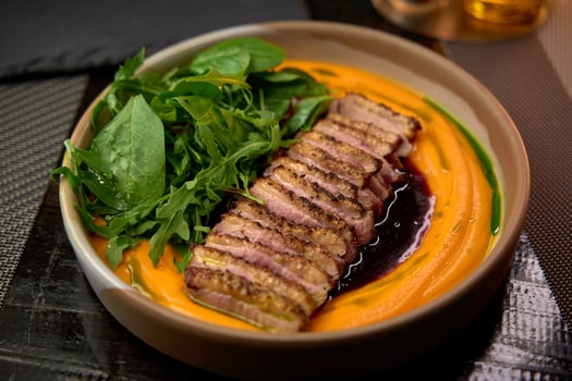 A beautifully plated dish featuring tender, seared duck breast served on a vibrant carrot puree with fresh greens, highlighting culinary artistry and flavor balance. photo