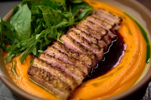 Deliciously Plated Dish Featuring Sliced Duck Breast Over Vibrant Puree Accompanied by Fresh Greens in a Gourmet Presentation photo