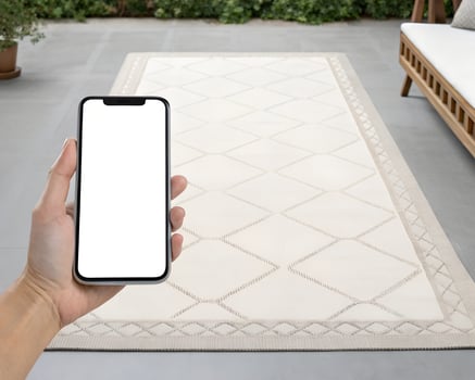 Hand Holding Smartphone Displaying Blank Screen Near Off White Geometric Rug on Patio photo
