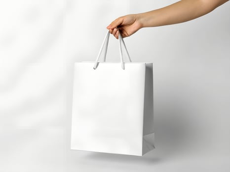 Woman's Hand Holding a Blank White Paper Shopping Bag Against a White Background photo