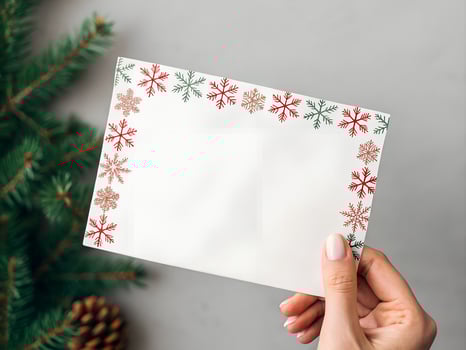 Woman Holding Blank White Christmas Card with Red and Green Snowflakes on Gray Background photo
