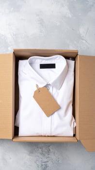White Shirt Folded Neatly in a Cardboard Box with Tag on Light Gray Background photo