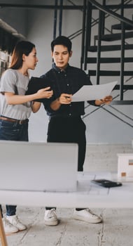 Two people standing in front of a laptop and looking at a blueprint photo