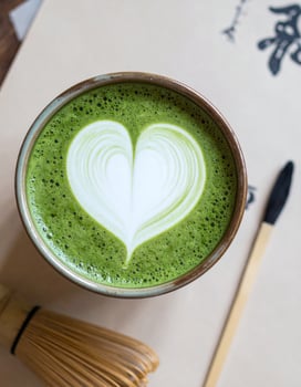 Matcha Latte with Heart Shaped Foam Art in Rustic Bowl on Beige Table photo