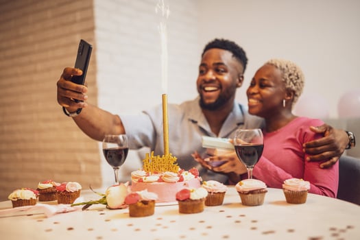 A young African American couple embraces as they take a joyful selfie together during a birthday celebration, with a cake and fireworks. photo