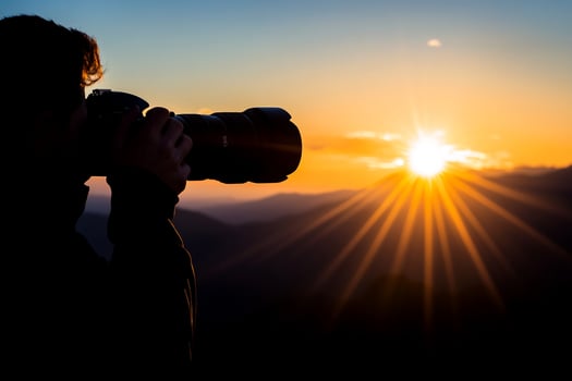 A person taking a photo of the sun setting over mountains